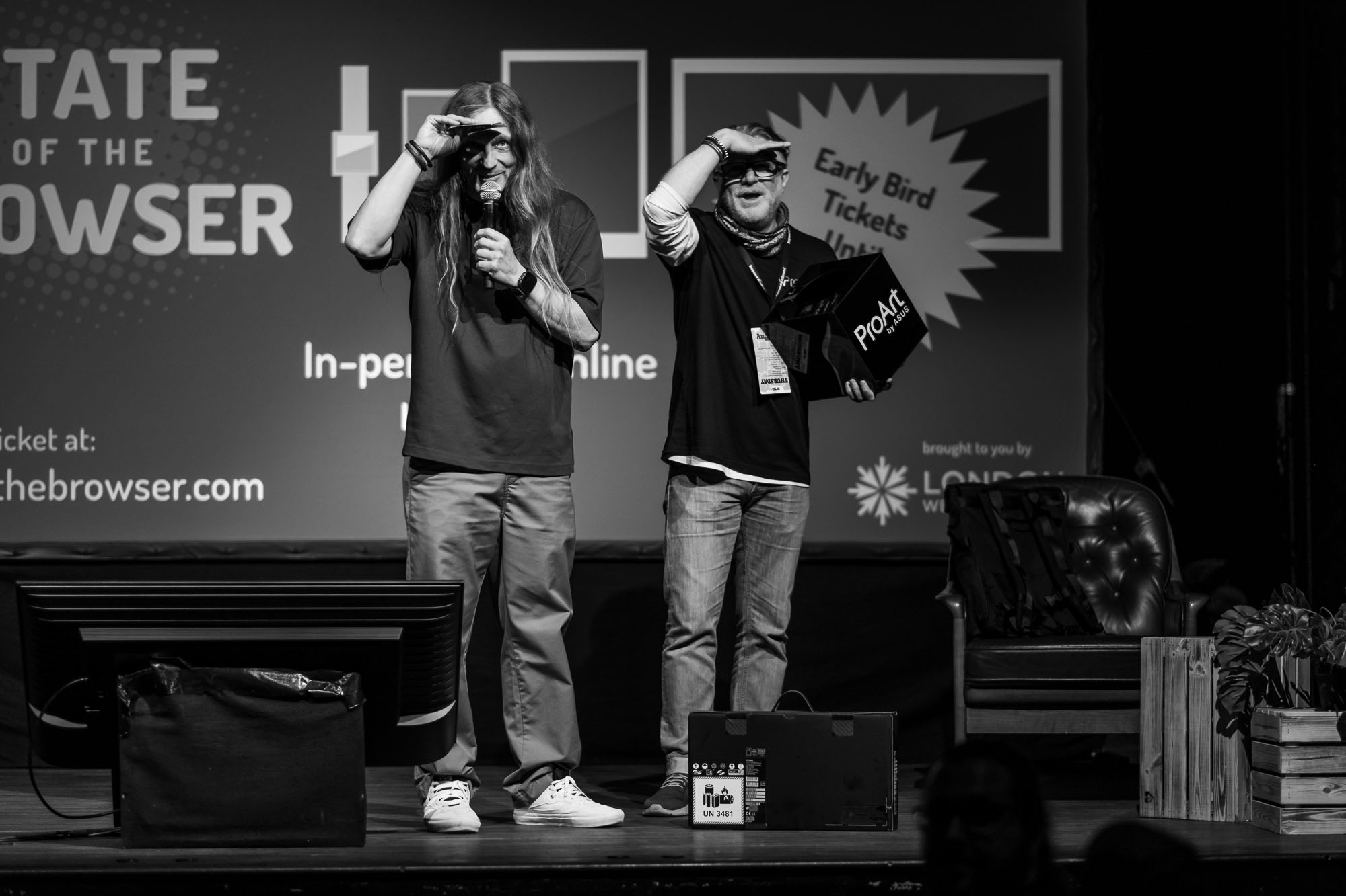 Two people standing on stage at beyond tellerrand with their hands above their eyes as if they search for someone and are blinded by the lights on stage.