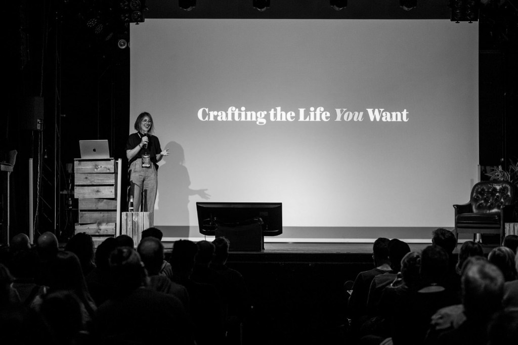 A black and white photo of Jessica Hische on stage at beyond tellerrand in Berlin. She is opening her talk in that moment and the slide in the back of her says “Crafting the life you want”.