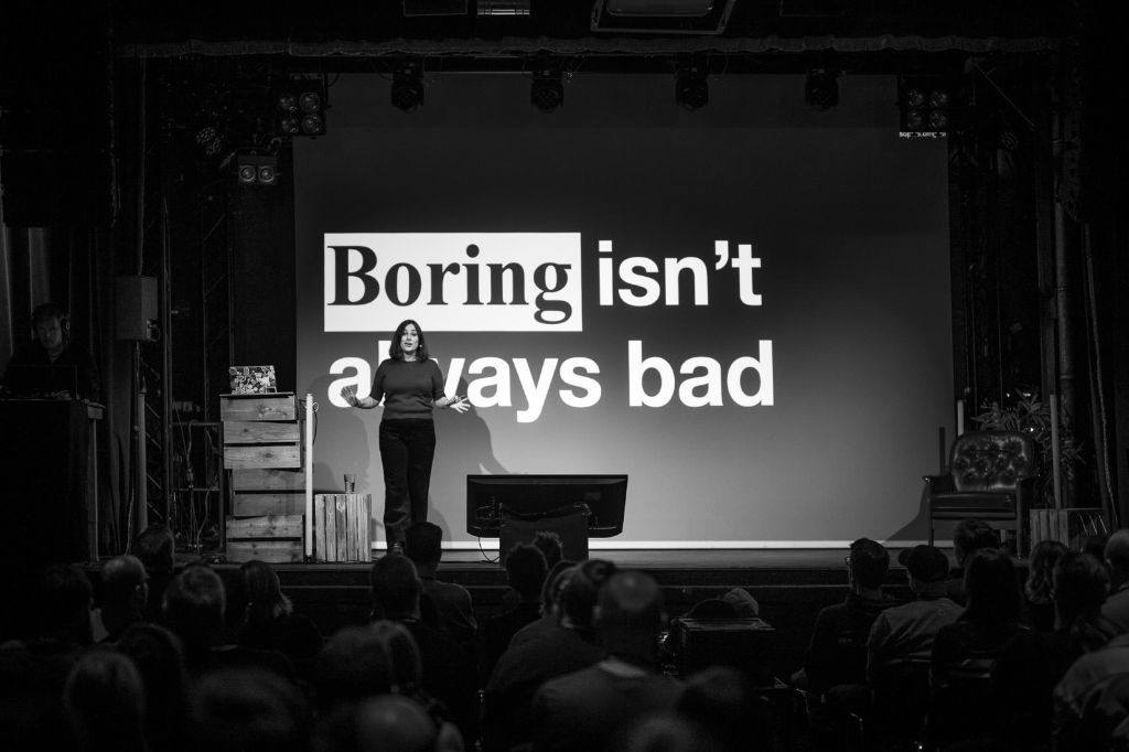 A black and white photo of Sophie Koonin on stage at beyond tellerrand in Berlin. The slide in her back says “Boring isn’t always bad”