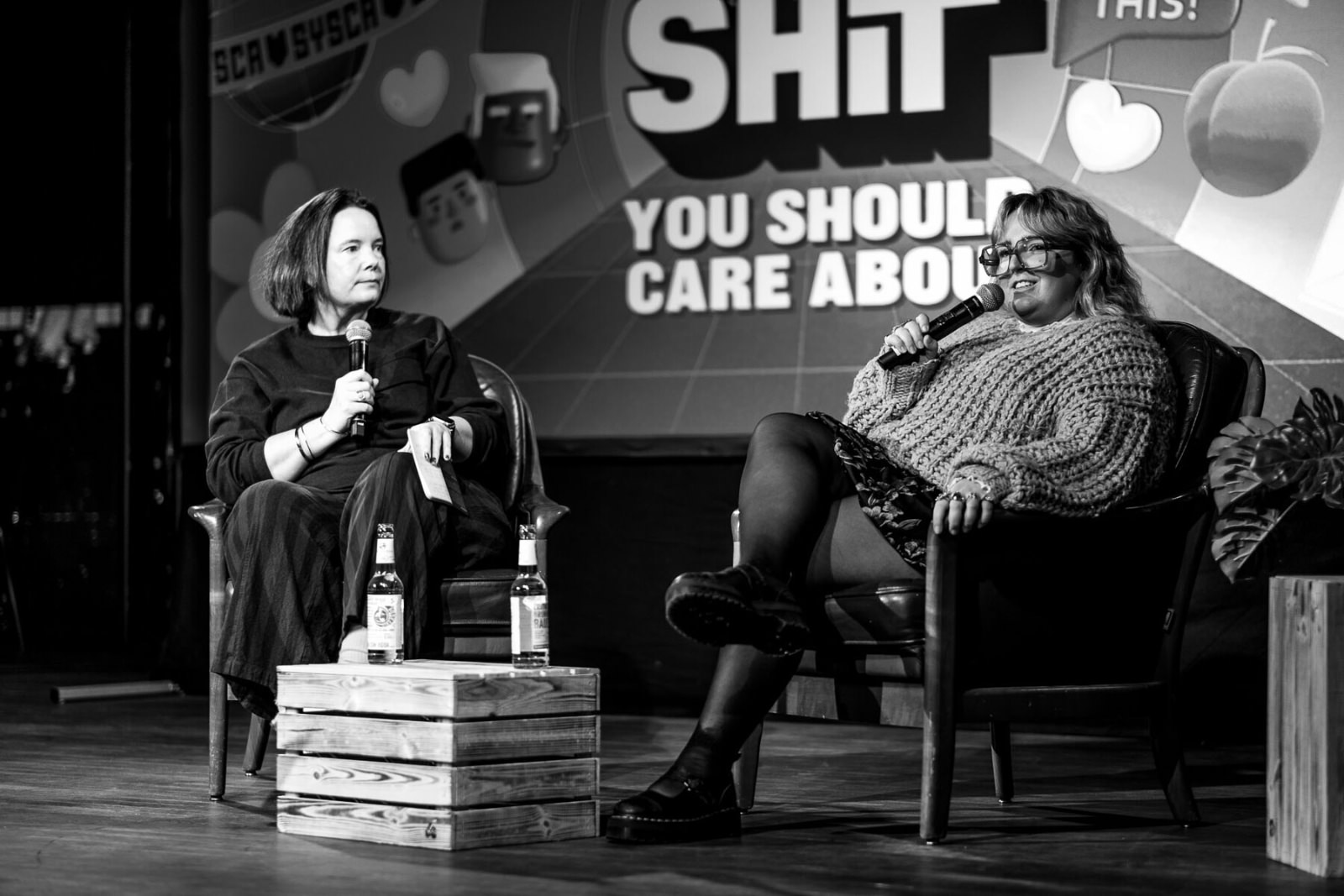 A black and white photo from the stage at beyond tellerrand Berlin 2025. Left is Sacha Judd, right is Lucy Blakiston. Both sitting on a comfy armchair. The slide in the background says &ldquo;Shit You Should Care About&rdquo;.