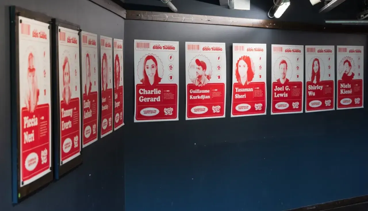 The photo shows a set of individual posters for each speaker hanging on a black wall. Printed in red on white paper.
