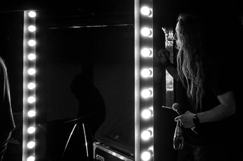 Marc standing backstage behind the curtain. You can see parts of the light bulbs that surround the stage.
