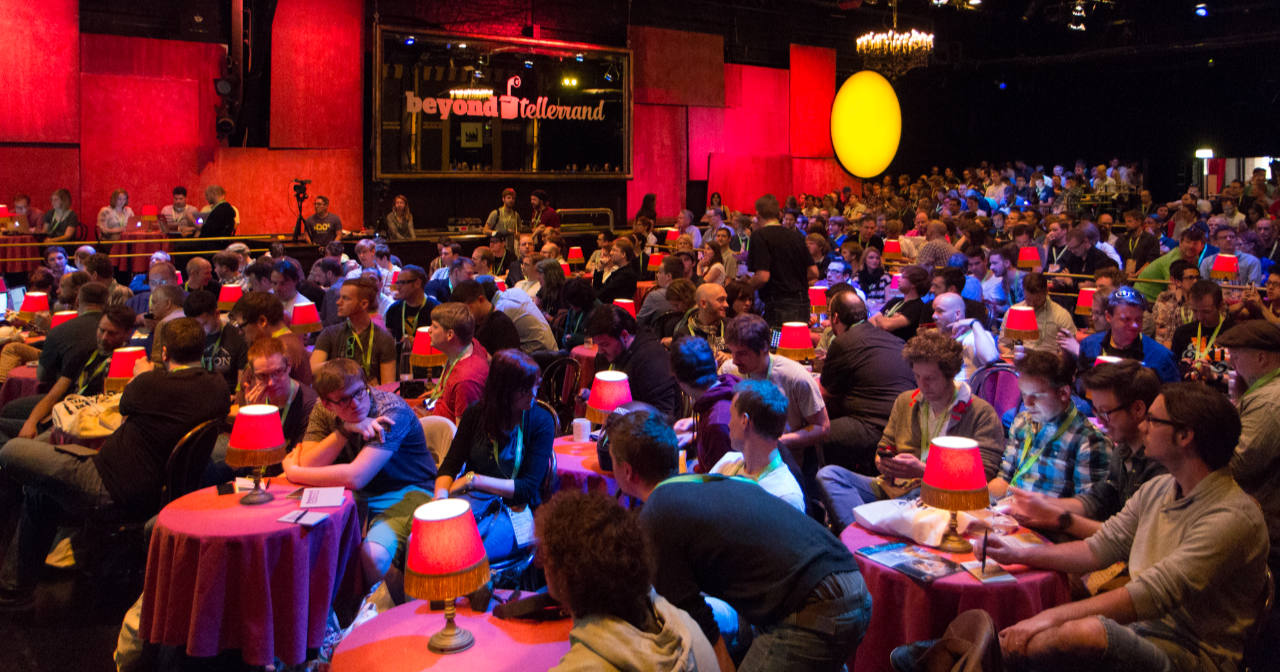 The audience of the 4th beyond tellerrand in 2014 in a photo taken from the ride side of the stage looking into the theatre. Red and warm lights are creating the warm atmosphere in this photo.