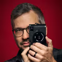 A portrait of Florian Ziegler. Photographer at beyond tellerrand, holding his camera in front of the right half of his face.