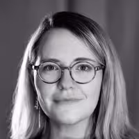 A portrait of Geri Coady. She wears glasses and firmly smiles into the camera