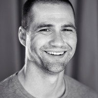 A portrait photo of Tim Kadlec. He has a massive smile on his face, short shaved, dark hair and a three-day beard.