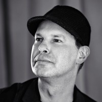 A portrait of the artist Noma Bar. He does not look into the camera, but to the upper left of the photo as if something was outside of the frame. Noma is grinning.