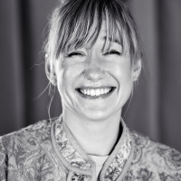 This is a portrait photo of Linda Liukas. She looks into the camera and has a big smile on her face. Looks very happy.