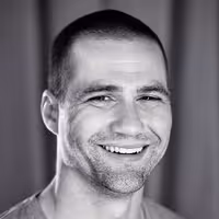 A portrait photo of Tim Kadlec. He has a massive smile on his face, short shaved, dark hair and a three-day beard.