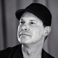 A portrait of the artist Noma Bar. He does not look into the camera, but to the upper left of the photo as if something was outside of the frame. Noma is grinning.