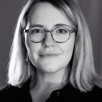 A portrait of Geri Coady. She wears glasses and firmly smiles into the camera
